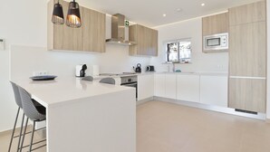 A modern kitchen with white cabinetry, a central island with bar stools, a microwave, and pendant lighting. - Waterside Village Townhouse (Luz)