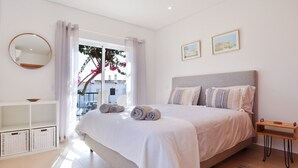 A bedroom with a bed, a bedside table, a mirror, and a window with curtains. - Waterside Village Townhouse (Luz)