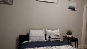 A bedroom with a bed, two pillows, a bedside table with a plant, and two framed pictures on the wall. - lovely relaxing room with hight speed internet , neflix with a independent entry (Goose Creek)