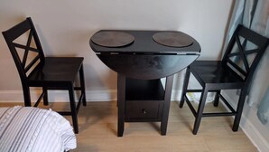 A small, dark-colored room with a single bed, a table with two chairs, and a small drawer. - lovely relaxing room with hight speed internet , neflix with a independent entry (Goose Creek)
