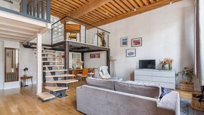 Un amplio salón con una escalera que conduce a un nivel superior, un sofá, un televisor y un comedor.