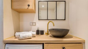 Un baño con tocador de madera, un lavabo de diseño, grifo dorado, espejo y lavadora integrada.