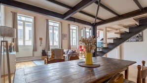 Un comedor amplio con una mesa de madera, sillas y un jarrón amarillo con flores secas.