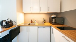 Una cocina compacta con armarios blancos, un lavamanos, una cafetera y un lavavajillas.