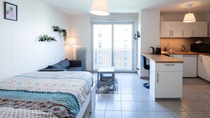 Un apartamento moderno con cama, una pequeña mesa, balcón, kitchenette y comedor.