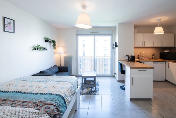 Un apartamento moderno con cama, una pequeña mesa, balcón, kitchenette y comedor.