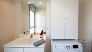 Un baño moderno con lavamanos, espejo y mueble blancos, lavadora integrada y un inodoro.
