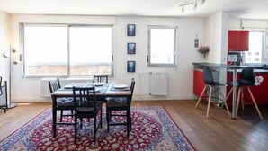 A modern apartment with a dining area, kitchen, and large windows.