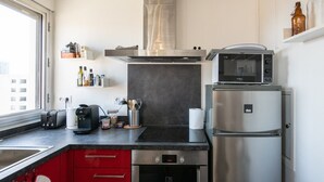 A modern kitchen with a stainless steel refrigerator, a microwave, and a built-in oven. There is a window providing natural light, and the kitchen features red cabinets and a black countertop.