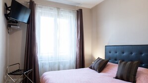 Hotellihuone, jossa on sänky, seinälle asennettu televisio ja ikkuna, jossa on verhot.