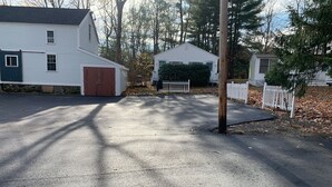 Une allée menant à une propriété résidentielle, avec deux maisons blanches, un garage et une clôture blanche à piquets.