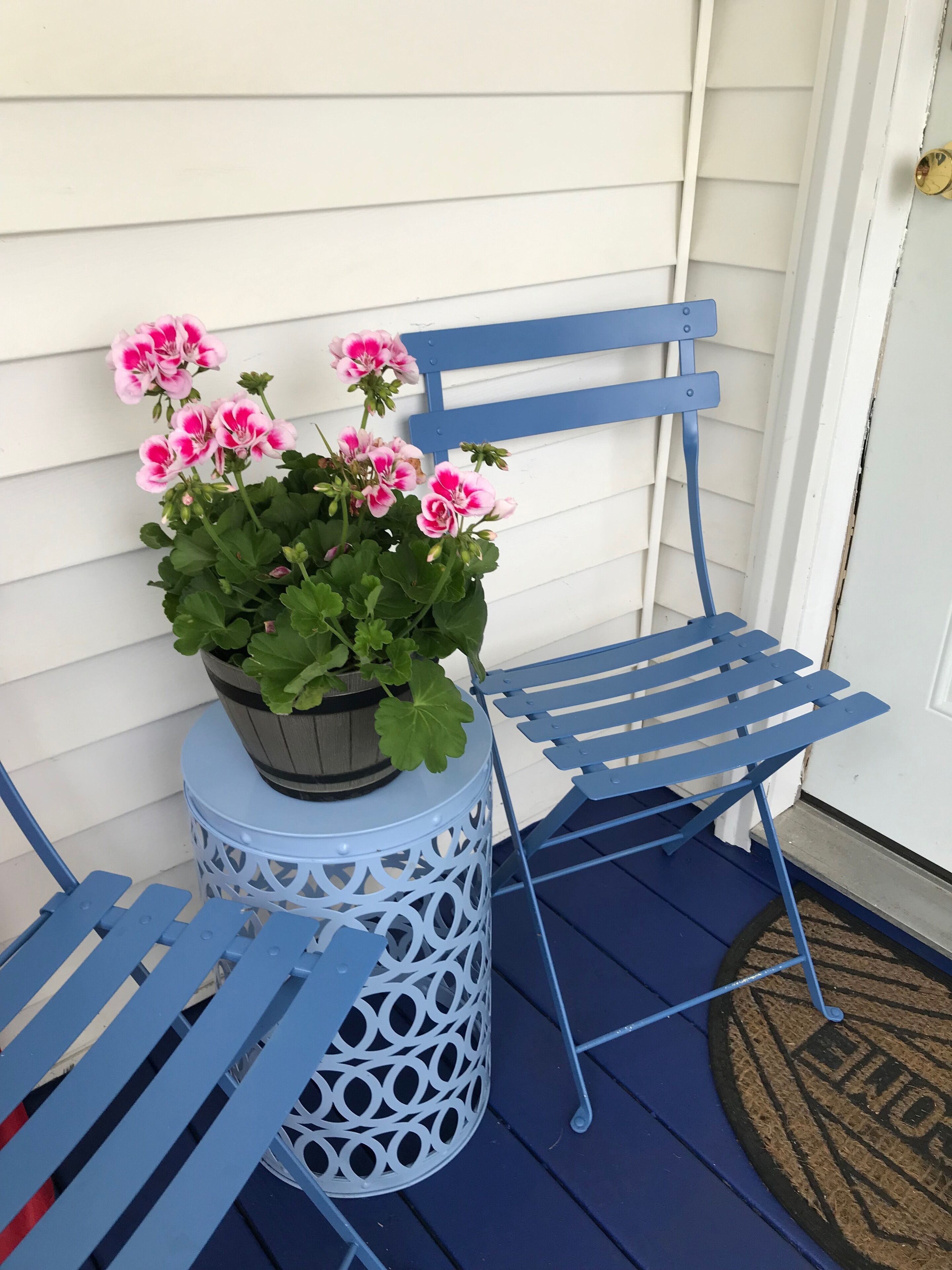 A blue metal chair with a potted plant of pink flowers on a white metal stool.