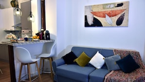 Una sala moderna con un sofá azul, sillas blancas y una zona de cocina con una mesa de comedor.