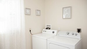 A laundry room with two white washing machines, a power outlet, and three framed floral wall art pieces. - Large 4 Bedroom CT Home Comfy for Longer Stay (Bristol)
