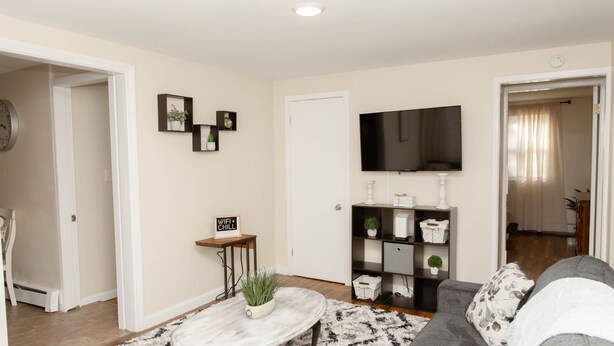 A living room with a sofa, a coffee table with a plant, a TV on the wall, and a bookshelf. - Large 4 Bedroom CT Home Comfy for Longer Stay (Bristol)