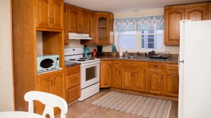A kitchen with wooden cabinets, a white stove, a microwave, and a window with patterned curtains. - Large 4 Bedroom CT Home Comfy for Longer Stay (Bristol)
