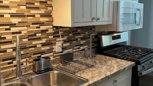Una cocina con armarios blancos, un lavamanos de acero inoxidable, un microondas y una estufa a gas.