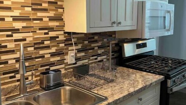 A kitchen with white cabinets, a stainless steel sink, a microwave, and a gas stove.