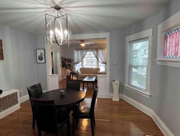 A dining area with a round table and chairs, a chandelier, and a view of a living room with a sofa and curtains. - Beautiful furnished 2 bdr great location Elmwood (Buffalo)