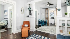 Un salon spacieux doté d’un parquet, d’un tapis à motifs bleus, d’un fauteuil turquoise et d’un coin repas avec des chaises bleues et une table blanche.