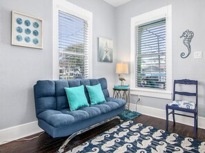 Una sala de estar con un sofá azul, cojines color turquesa, un tapete estampado, una mesita de noche con una lámpara y una silla con diseño azul y blanco.