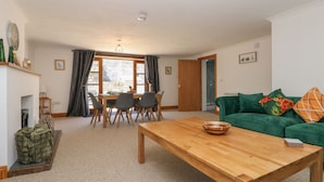 Ein Wohnzimmer mit Couchtisch aus Holz, einem grünen Sofa und einem Essbereich mit Tisch und Stühlen.