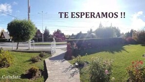 A residential street scene with a paved pathway, greenery, and a white fence. - Hotel Ariel (El Calafate)