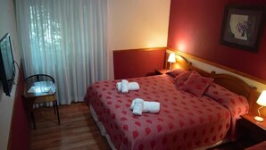 A hotel room with two beds, a chair, a desk, and a lamp. - Hotel Ariel (El Calafate)