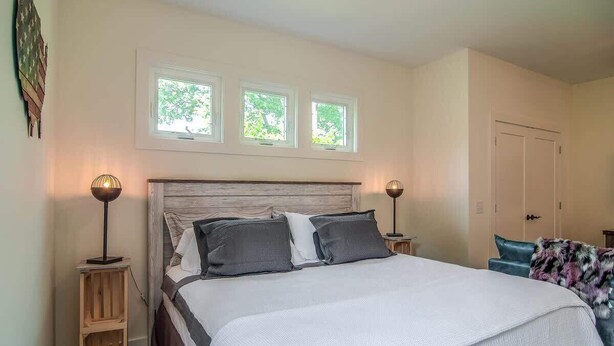 A bedroom with a large bed, two bedside lamps, a wooden headboard, and a window above the bed. - Rustic Studio Walkable to Music Row (Nashville)