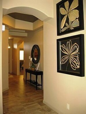 A hallway with wooden flooring, a black console table with decorative items, and two framed wall art pieces.