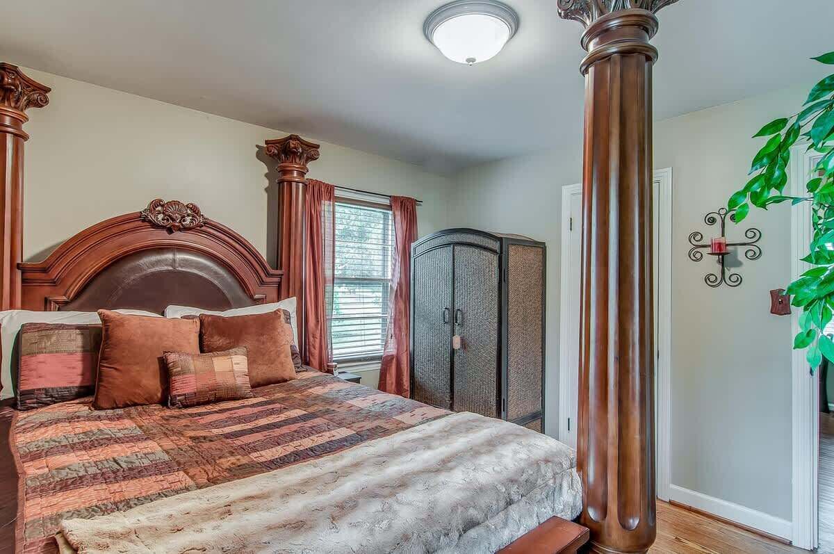 Ein Schlafzimmer mit einem großen Bett, einem Holzkopfende, einem Kleiderschrank und einer Pflanze.