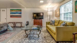 Uma sala de estar com sofá, mesa de centro, televisão e um quadro na parede.