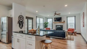 A modern kitchen with a central island, a dining area with a sofa, and a TV mounted on the wall. - The Sage Estate - Only 6 Minutes from Downtown (Nashville)