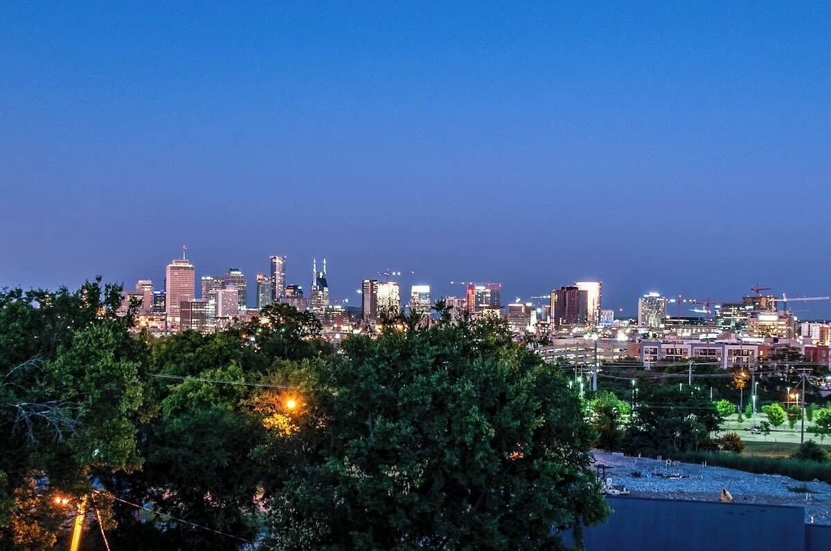 A city skyline at dusk with illuminated buildings and a park in the foreground.