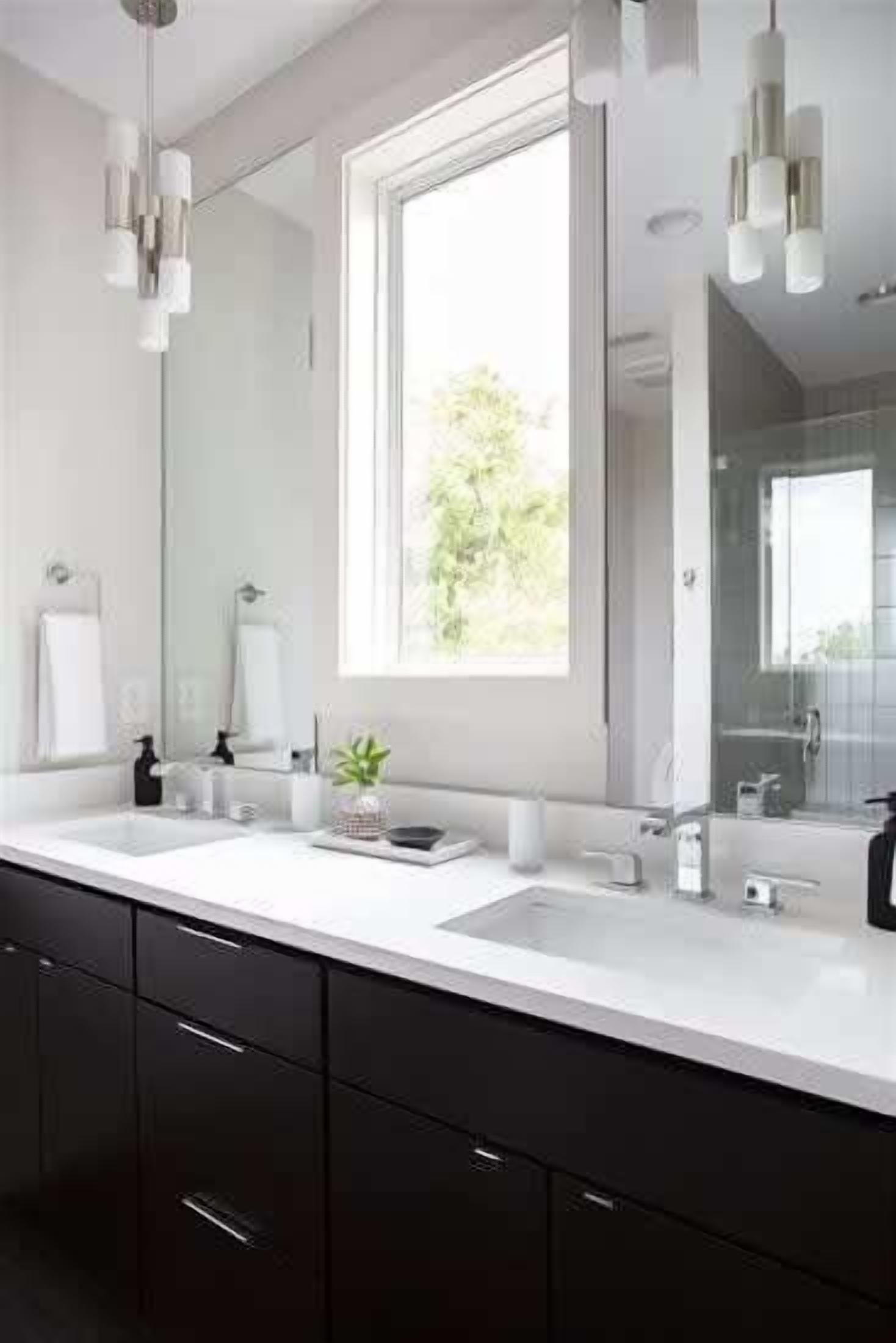 A modern bathroom with a large mirror, two sinks, and a window providing natural light.