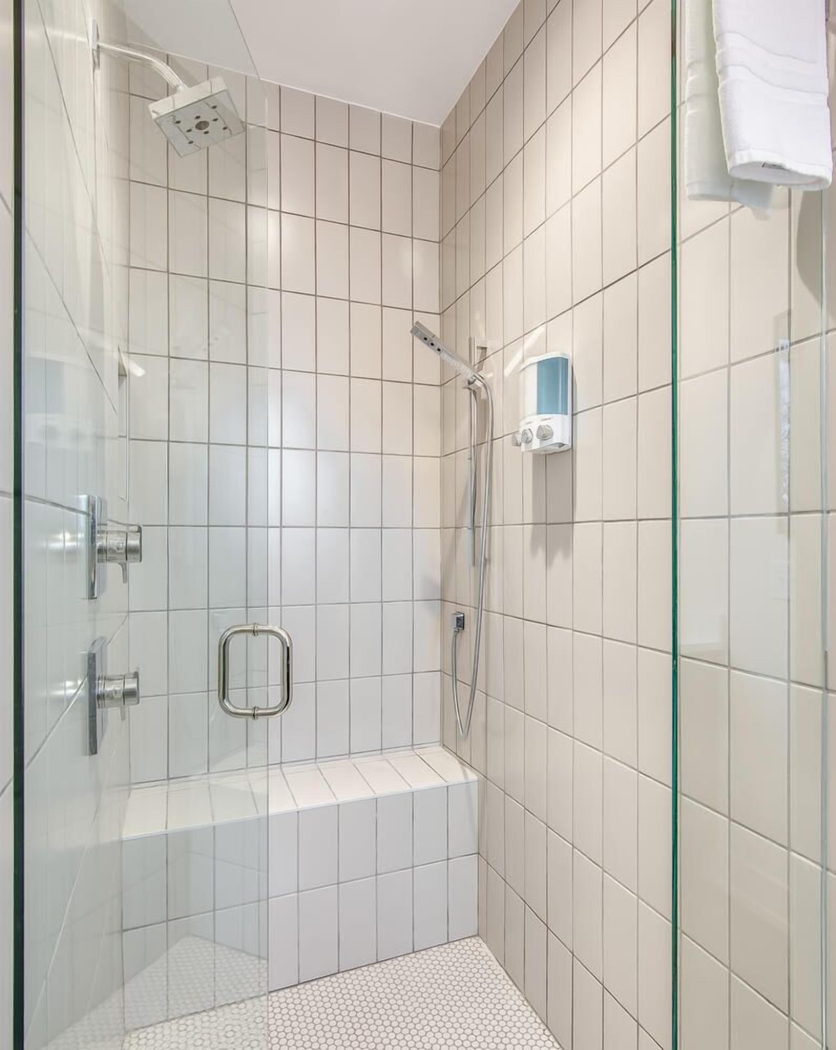 A modern shower area with a glass door, a handheld showerhead, and a wall-mounted control panel.
