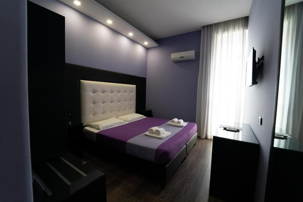 A modern hotel room with a large bed, a bedside table, a dresser, and a TV mounted on the wall.
