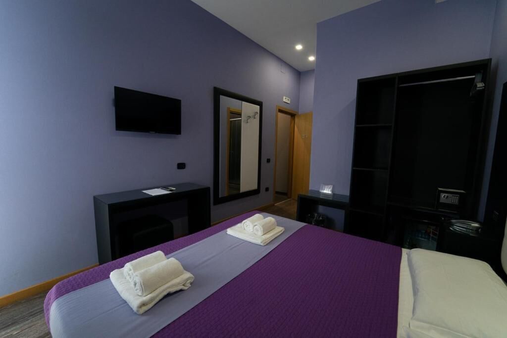 A hotel room with a bed, a desk, a mirror, and a television.