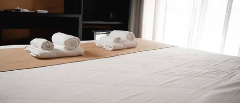 Una habitación de hotel con una cama bien hecha, cabecera de madera y un gran ventanal con cortinas.