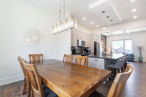 A modern kitchen with a central island, wooden dining table, and chairs. - The East Side Vibe- Modern East Nash Stay, Garage & Open Living + Great Location (Nashville)