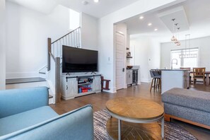 A modern living room with a flat-screen TV, a staircase, a kitchen area, and a dining space. - The East Side Vibe - Spacious Home in Great (Nashville)