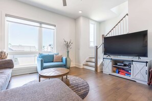 A living room with a sofa, a coffee table, a TV, and a staircase. - The East Side Vibe- Modern East Nash Stay, Garage & Open Living + Great Location (Nashville)