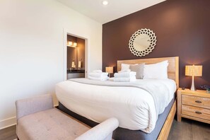 A modern hotel room with a large bed, a bedside table with a lamp, and a chair.
