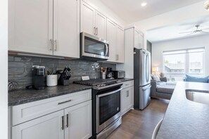 Una cocina moderna con armarios blancos, microondas integrado, refrigerador de acero inoxidable y estufa a gas.