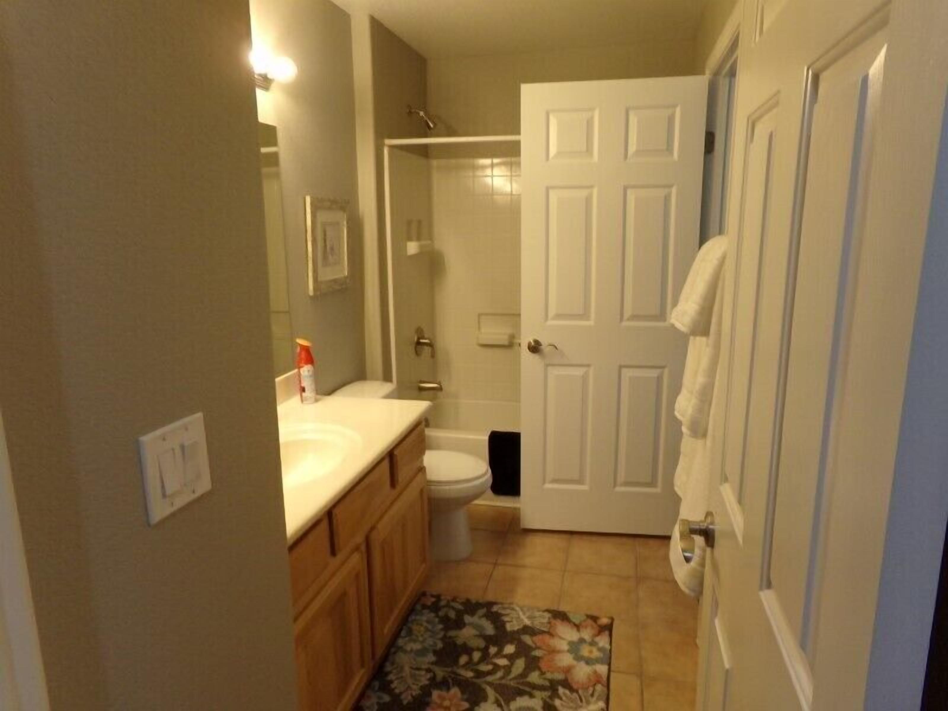 A bathroom with a toilet, sink, shower, and a door with a towel hanging on it.