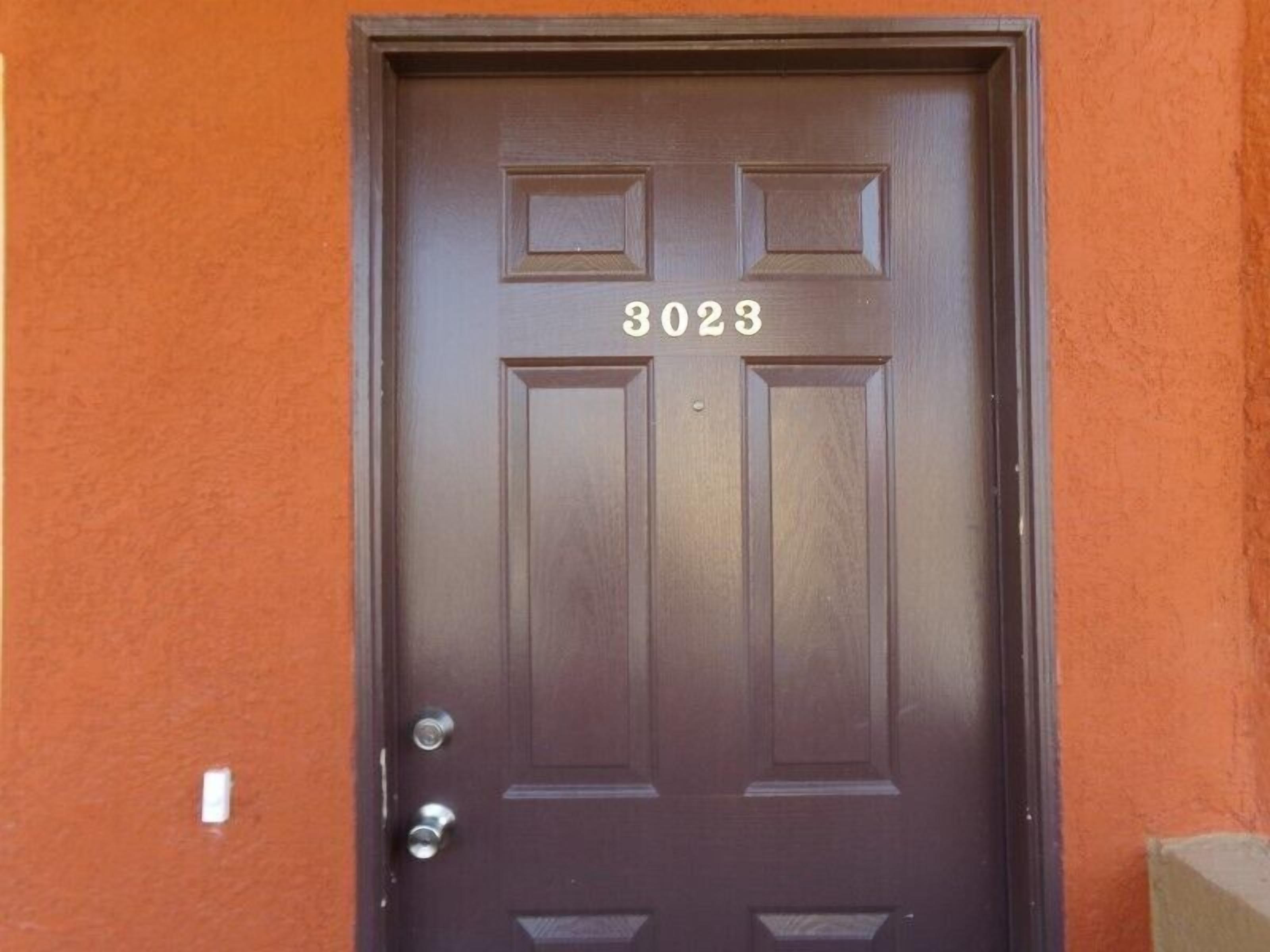 A dark brown door with the number 3023 on it, set in a textured orange wall.