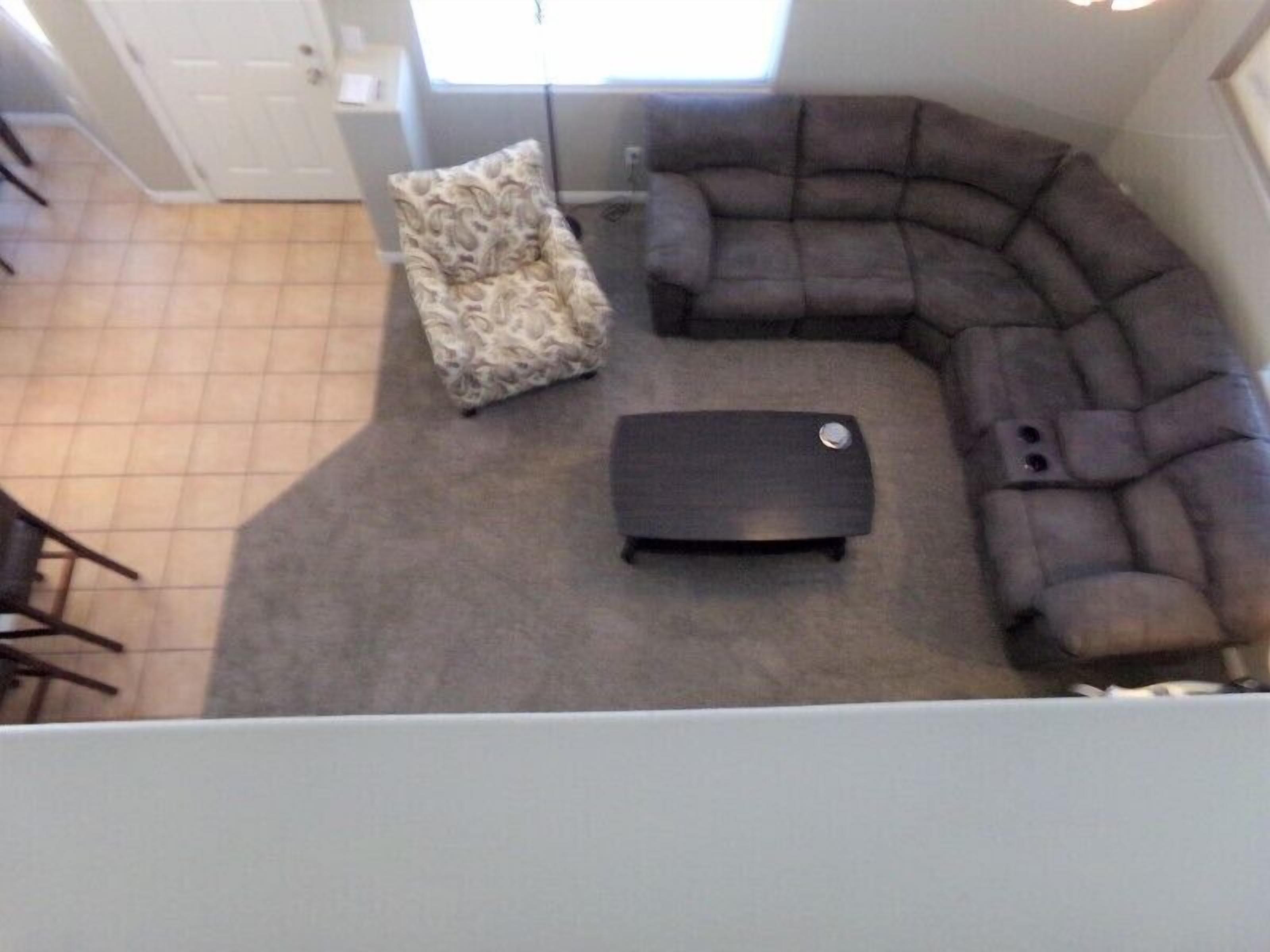 A living room with a sectional sofa, a patterned armchair, and a small ottoman.