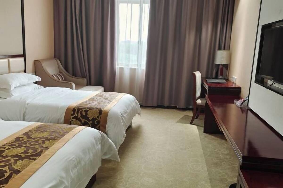 A hotel room with two beds, a desk, a chair, a TV, and a window with curtains.