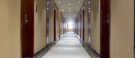 Un largo y estrecho pasillo de hotel con puertas a ambos lados, que conduce a habitaciones individuales.