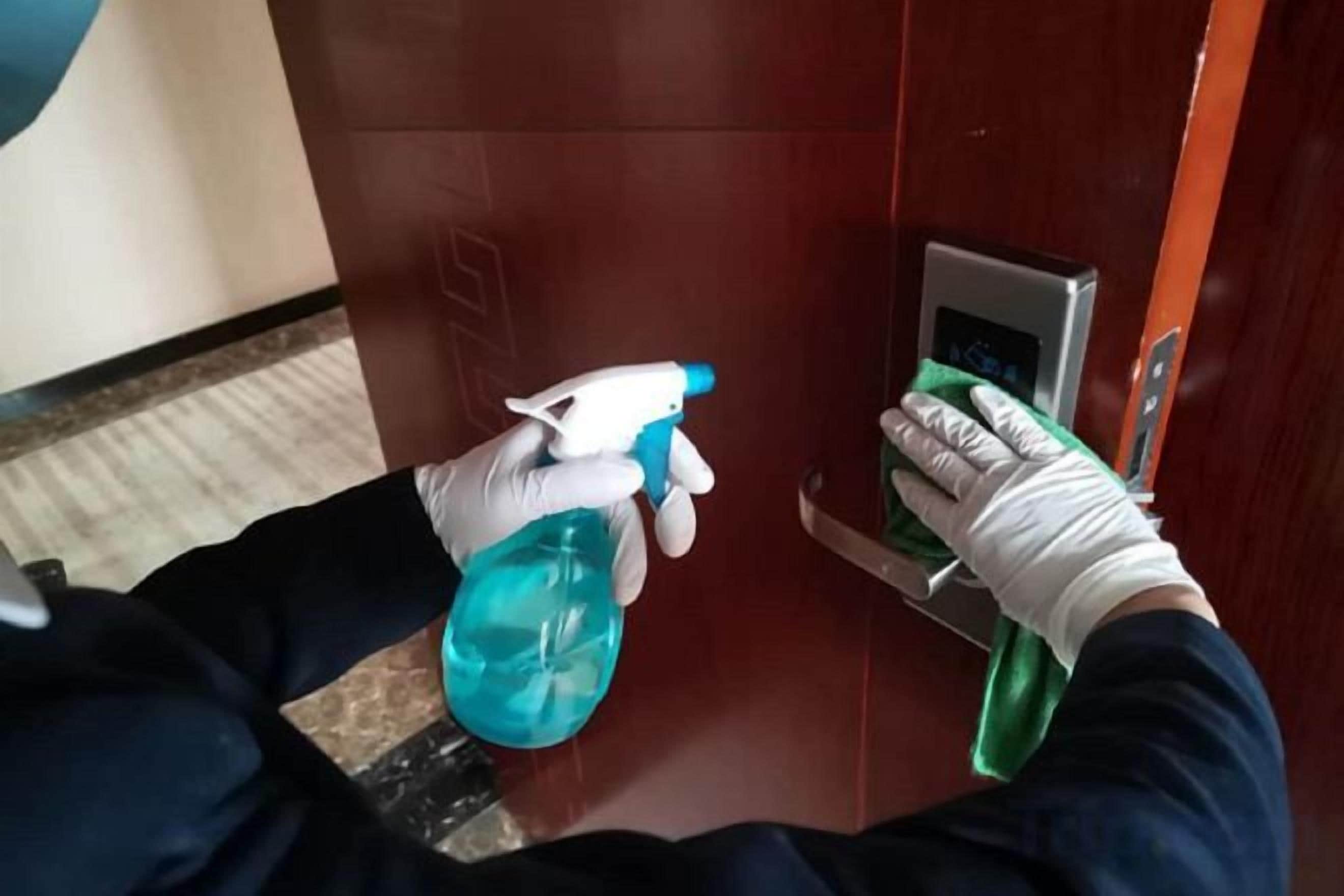 Una persona usa un flacone spray e uno straccio per pulire una maniglia.